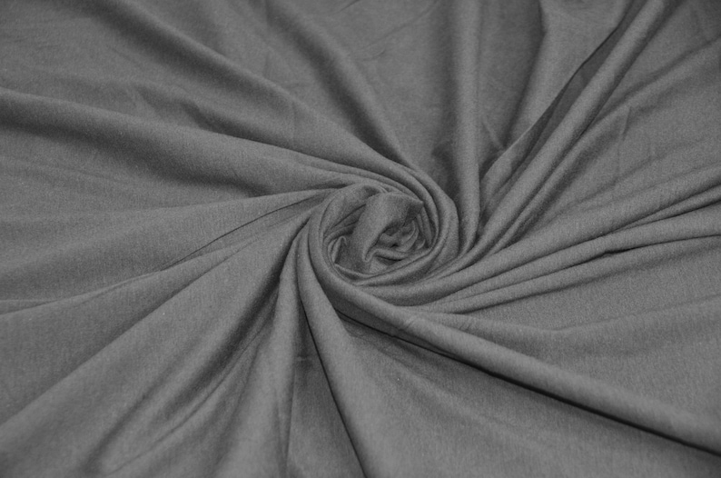 May include: A close-up of a gray fabric with a soft, smooth texture. The fabric is folded and twisted, creating a swirling pattern.