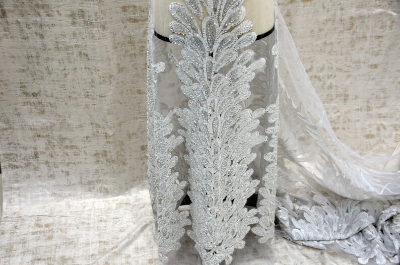 Puede incluir: Tela de encaje blanca con cuentas con un delicado patr&oacute;n floral. La tela es transparente y tiene una textura suave y fluida.
