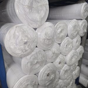 Puede incluir: Una pila de rollos de tela blanca envueltos en pl&aacute;stico transparente, probablemente para proyectos de costura o acolchado.