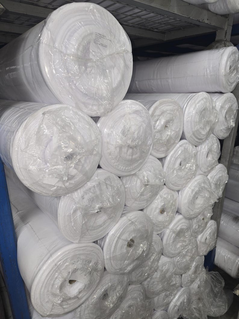 Puede incluir: Una pila de rollos de tela blanca envueltos en pl&aacute;stico transparente, probablemente para proyectos de costura o acolchado.