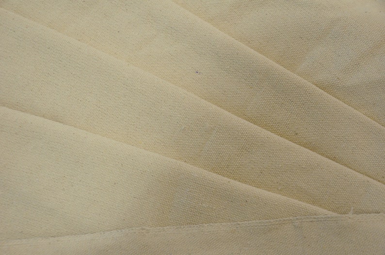 May include: Close-up of a folded piece of natural-colored canvas fabric. The fabric has a smooth, even texture and a subtle sheen.