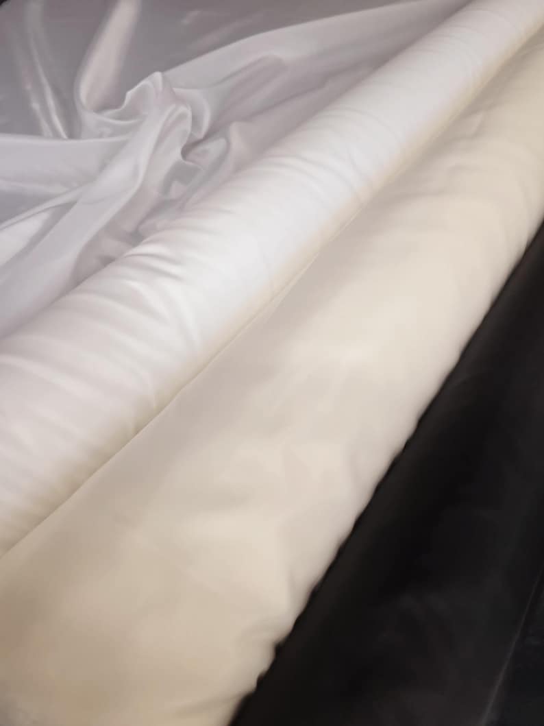 Puede incluir: Dos rollos de tela blanca, uno encima del otro. El rollo superior es transparente y el rollo inferior es opaco.