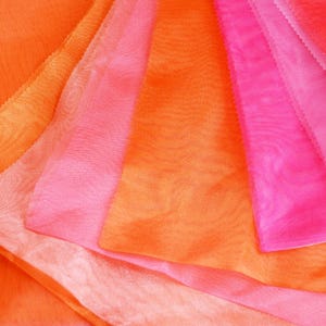 May include: A stack of sheer fabric in various shades of orange and pink. The fabric is layered and overlapping, creating a soft and delicate look.