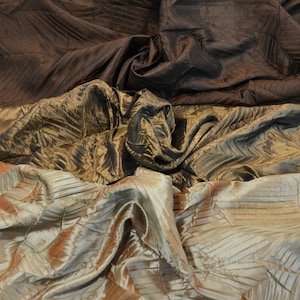 May include: A close-up of three layers of fabric. The top layer is a dark brown, the middle layer is a gold and brown patterned fabric, and the bottom layer is a light brown and gold patterned fabric.