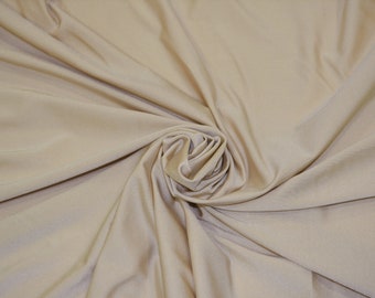 May include: A close-up of a smooth, beige fabric with a soft, silky texture. The fabric is draped and folded, creating a swirling pattern.