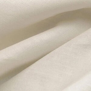 May include: Close-up of a smooth, off-white fabric with a subtle texture. The fabric is folded in a way that shows the drape and flow of the material.