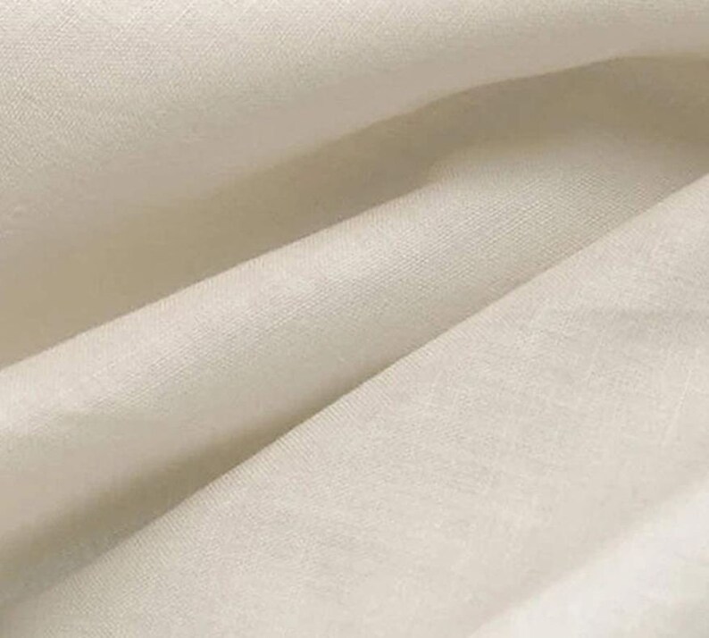 May include: Close-up of a smooth, off-white fabric with a subtle texture. The fabric is folded in a way that shows the drape and flow of the material.