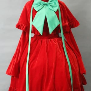 May include: A red velvet dress with a green bow and a matching cape. The dress has a ruffled hem and long sleeves.
