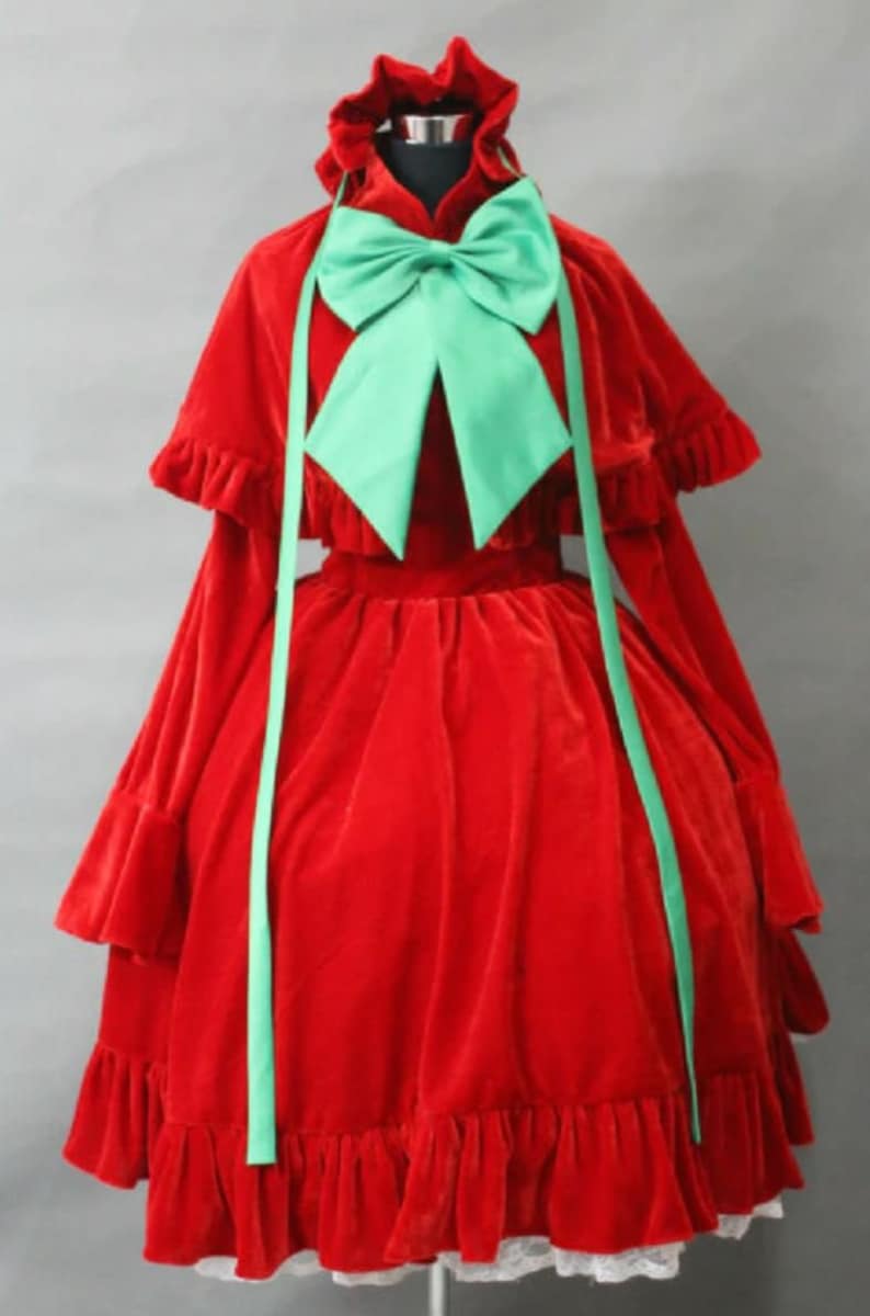 May include: A red velvet dress with a green bow and a matching cape. The dress has a ruffled hem and long sleeves.