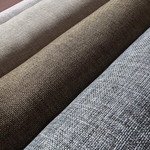May include: Close-up of several rolls of woven fabric in various neutral colors. The colors range from light pink to gray, with shades of beige and brown in between. The fabric has a textured appearance.
