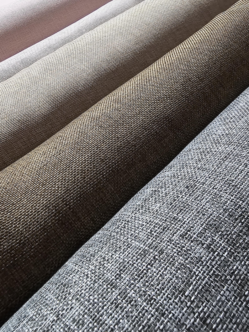 May include: Close-up of several rolls of woven fabric in various neutral colors. The colors range from light pink to gray, with shades of beige and brown in between. The fabric has a textured appearance.