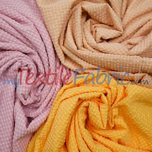 May include: Close-up of three swatches of textured fabric in pink, peach, and yellow. The fabric has a waffle-like pattern. The pink fabric is on the left, the peach in the middle, and the yellow on the bottom.