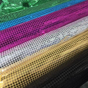 May include: Six rolls of iridescent fabric with a square grid pattern. The fabric is available in green, blue, pink, silver, gold, and black.