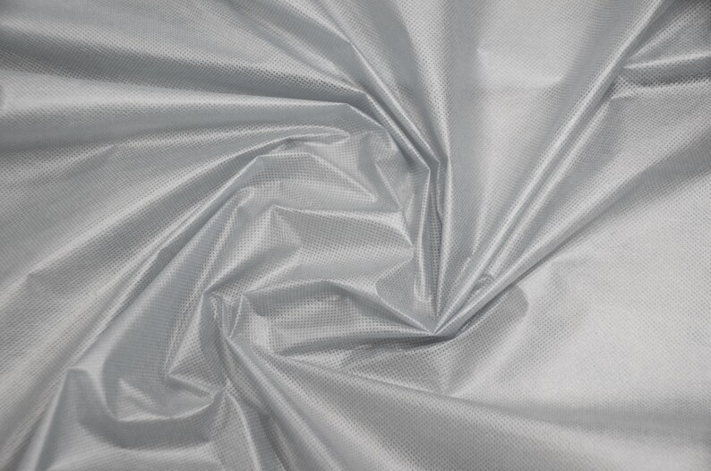May include: A close-up of a silver fabric with a subtle textured pattern. The fabric is wrinkled and folded, creating a soft, flowing look.