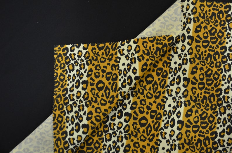 Op de afbeelding: Een close-up van een stof met een luipaardprint. De stof is een combinatie van beige, bruin en zwarte kleuren.
