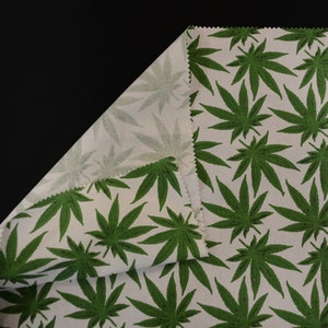 May include: White fabric with a green marijuana leaf pattern. The fabric is folded over to show the pattern on both sides.