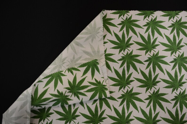 May include: White fabric with a green marijuana leaf pattern. The fabric is folded over to show the pattern on both sides.