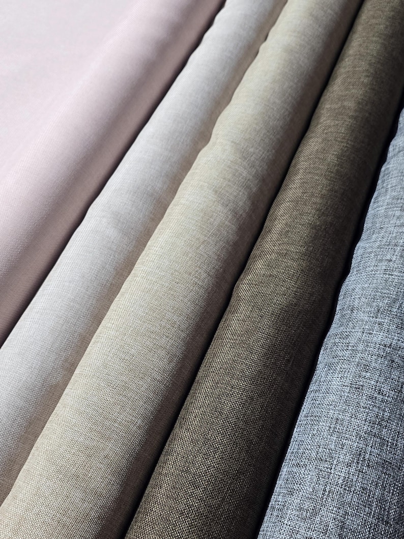 May include: Close-up of several rolls of fabric in various neutral colors. The fabrics range from light pink to gray, with textures that suggest linen or a similar woven material. The rolls are arranged diagonally.