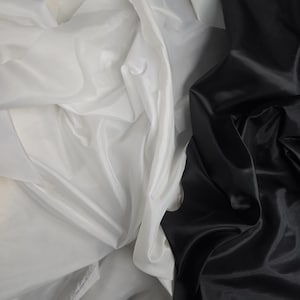 Puede incluir: Primer plano de dos telas, una blanca y otra negra, drapeadas y dobladas juntas. La tela blanca es transparente y la tela negra es lisa y brillante.