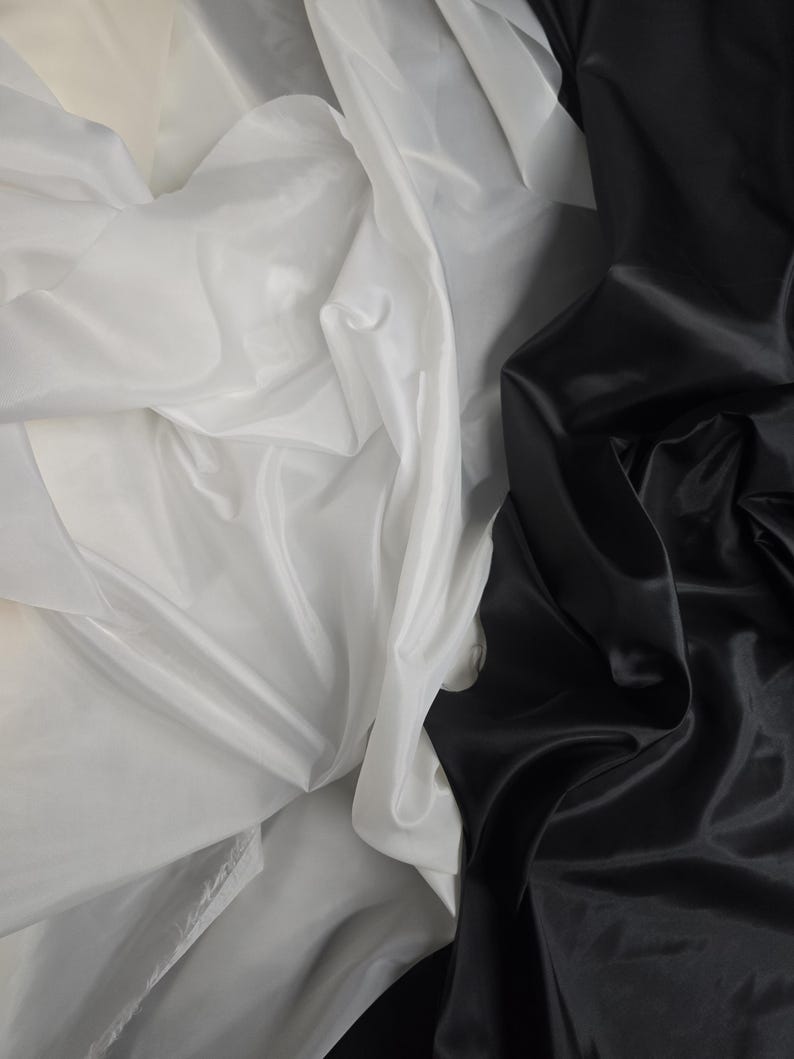 Puede incluir: Primer plano de dos telas, una blanca y otra negra, drapeadas y dobladas juntas. La tela blanca es transparente y la tela negra es lisa y brillante.