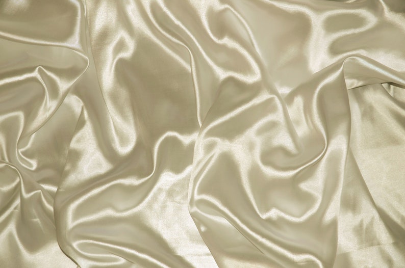 May include: A close-up of a smooth, ivory-colored satin fabric with soft, flowing folds and wrinkles.