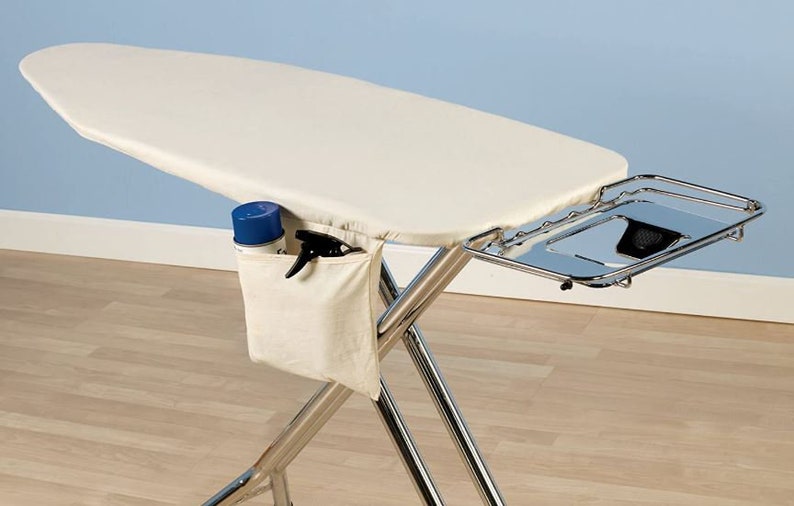 May include: A white ironing board with a chrome frame and a metal tray. The ironing board has a white fabric cover and a pocket on the side for storing ironing supplies. The tray is attached to the side of the ironing board and can be used to hold items like a spray bottle or iron.