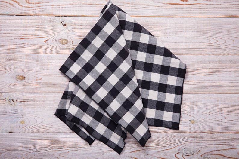 May include: A black and white checkered kitchen towel folded on a white wooden surface.