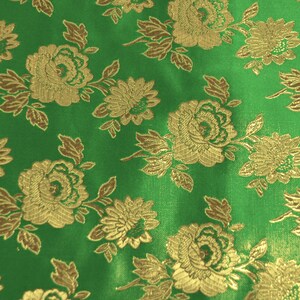 May include: Green fabric with a gold floral pattern. The fabric has a satin-like sheen and features a repeating design of roses and other flowers.