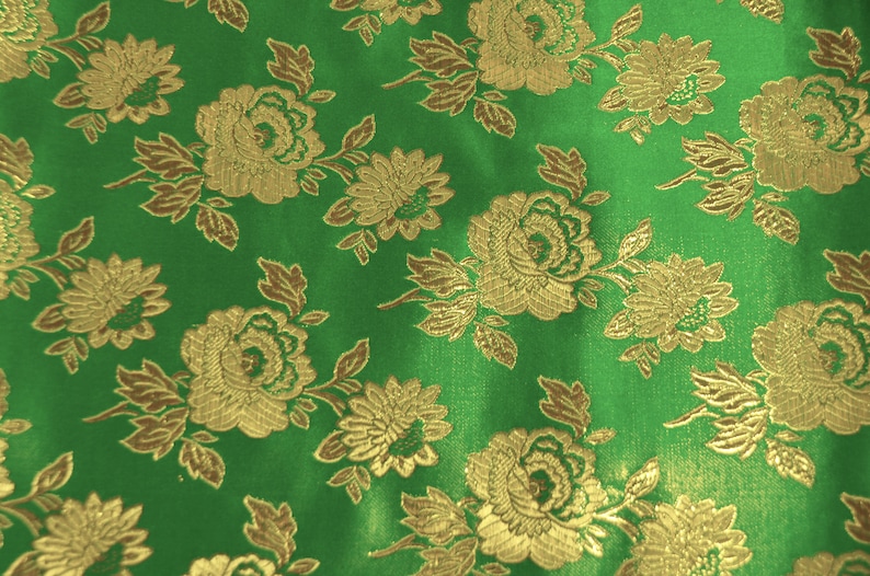 May include: Green fabric with a gold floral pattern. The fabric has a satin-like sheen and features a repeating design of roses and other flowers.