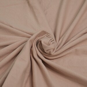 May include: A close-up of a soft, light brown fabric with a smooth texture. The fabric is folded and twisted into a spiral shape.