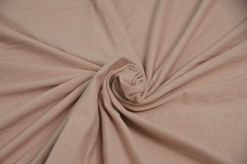 May include: A close-up of a soft, light brown fabric with a smooth texture. The fabric is folded and twisted into a spiral shape.