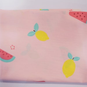 May include: Pink fabric with a repeating pattern of lemons and watermelon slices. The lemons are yellow with green leaves and the watermelon slices are red with black seeds and green rinds.