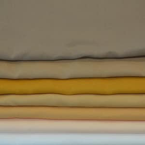 Peut inclure: Six échantillons de tissu empilés dans différentes nuances de beige, jaune et orange.