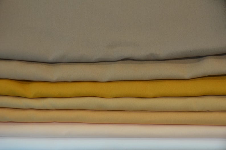 Puede incluir: Conjunto de seis muestras de tela apiladas en varios tonos de beige, amarillo y naranja.