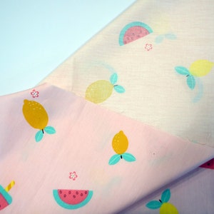 May include: Pink fabric with a repeating pattern of lemons, watermelons, and ice pops. The fabric is folded in half, showing the pattern on both sides.