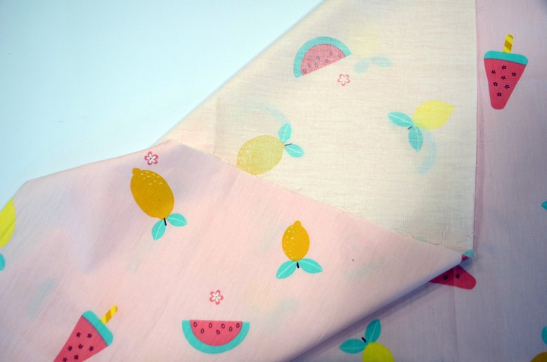 May include: Pink fabric with a repeating pattern of lemons, watermelons, and ice pops. The fabric is folded in half, showing the pattern on both sides.