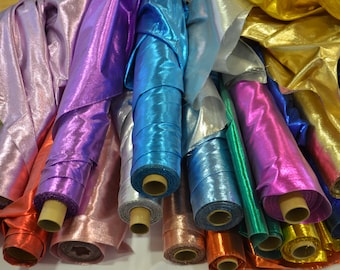 May include: Rolls of iridescent fabric in various colours, including purple, blue, green, gold, and silver. The fabric is rolled up and tied with brown string.
