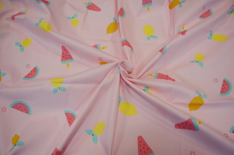 May include: Pink fabric with a repeating pattern of watermelon slices and lemons. The watermelon slices are red, green, and black, and the lemons are yellow with green leaves.