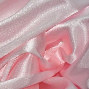 May include: A close-up of soft, pink satin fabric with a smooth, silky texture. The fabric is draped and folded, creating a luxurious and elegant look.
