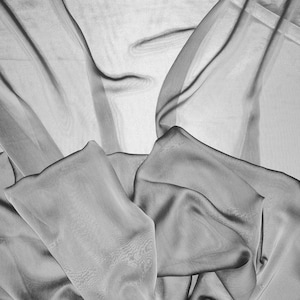 May include: A close-up of a sheer, gray fabric draped in soft folds. The fabric is translucent and has a subtle sheen.