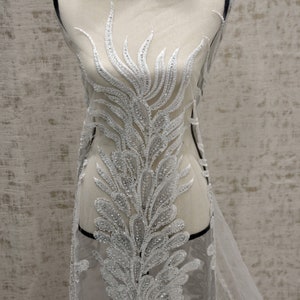 Puede incluir: Tela de encaje blanca con cuentas con un delicado patr&oacute;n floral. La tela es transparente y tiene una textura suave y fluida.