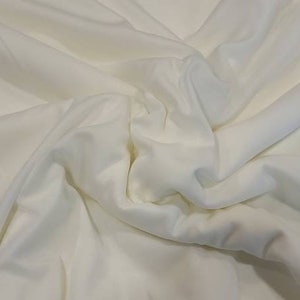 Puede incluir: Primer plano de una tela blanca con una textura suave. La tela est&aacute; drapeada y doblada, creando l&iacute;neas suaves y fluidas.