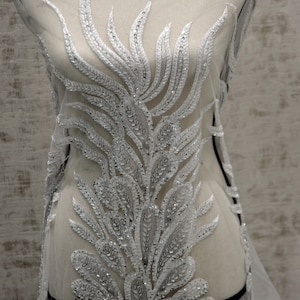 Puede incluir: Tela de encaje blanca con cuentas con un delicado dise&ntilde;o floral. La tela es transparente y tiene un brillo sutil.