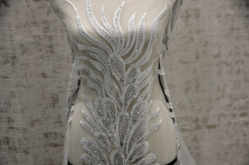 Puede incluir: Tela de encaje blanca con cuentas con un delicado dise&ntilde;o floral. La tela es transparente y tiene un brillo sutil.
