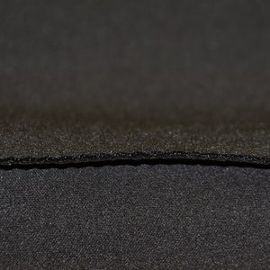 May include: Close-up of two layers of black fabric. The top layer has a textured surface, while the bottom layer is smooth.