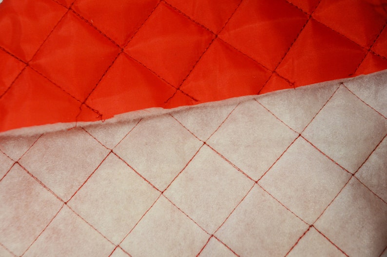 May include: Close-up of two quilted fabrics, one red and one white, with diamond-shaped stitching. The red fabric is on top of the white fabric.