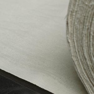 May include: Close-up of a white fabric roll, showing the texture of the material. The fabric is rolled up and the edge of the roll is visible.