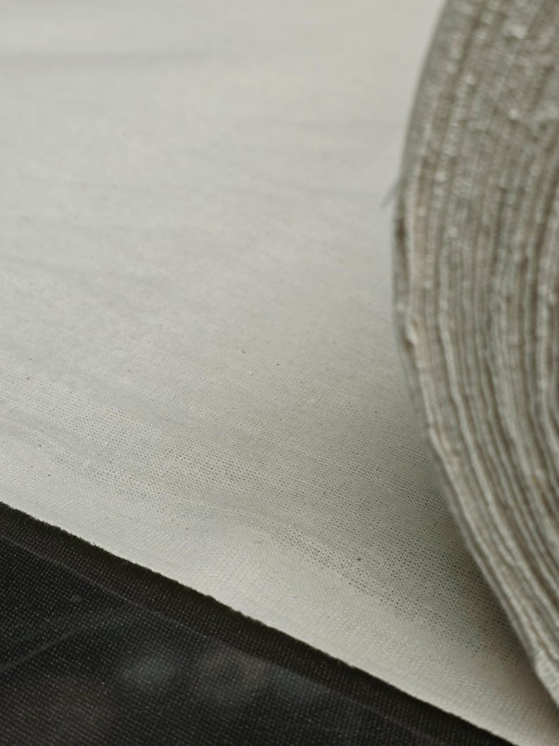 May include: Close-up of a white fabric roll, showing the texture of the material. The fabric is rolled up and the edge of the roll is visible.