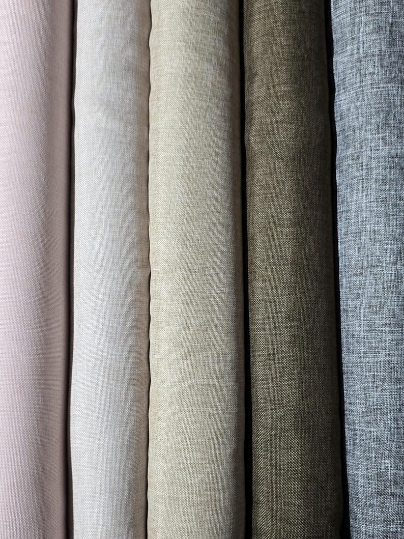 May include: A close-up of several rolls of fabric in various neutral colors. The colors range from a soft pink to a light gray-blue, with shades of white, beige, and olive green in between. The fabric has a textured appearance.