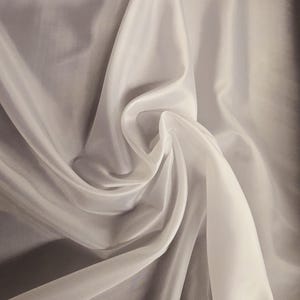 Puede incluir: Tela blanca transparente con una textura suave y fluida. La tela est&aacute; drapeada y doblada, creando un aspecto liso y elegante.